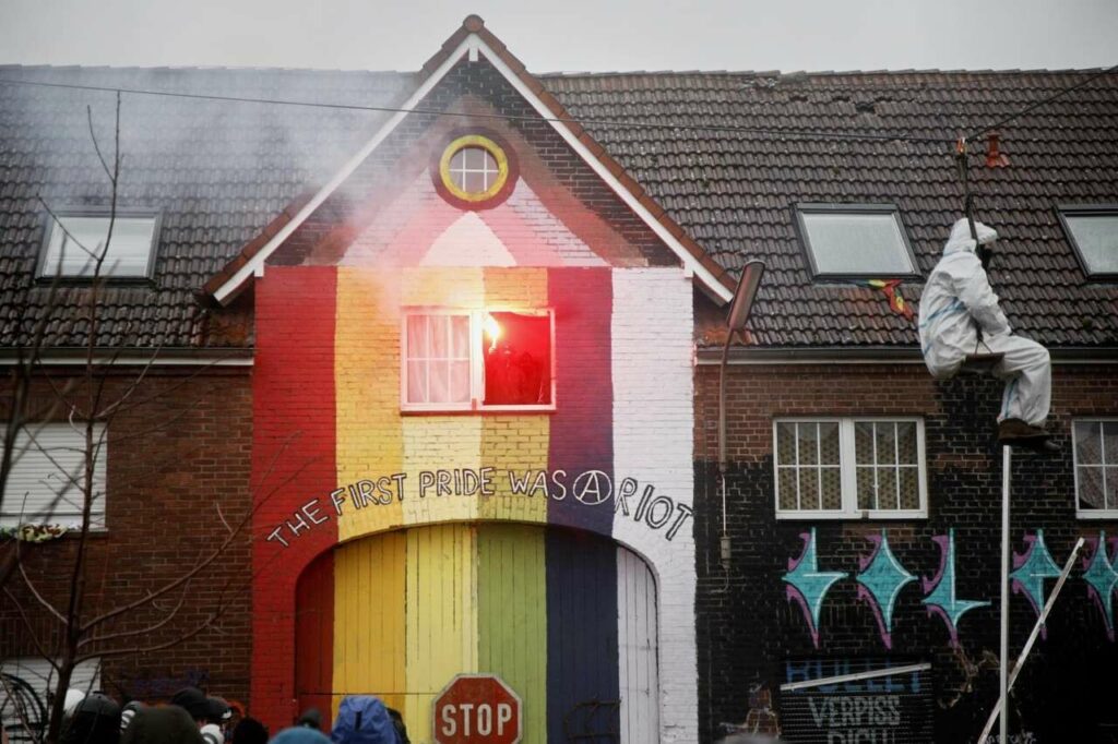 A two-story brick building, wide, with a tower-shaped entrance gate painted in rainbow colours and the words: The first pride was a riot.