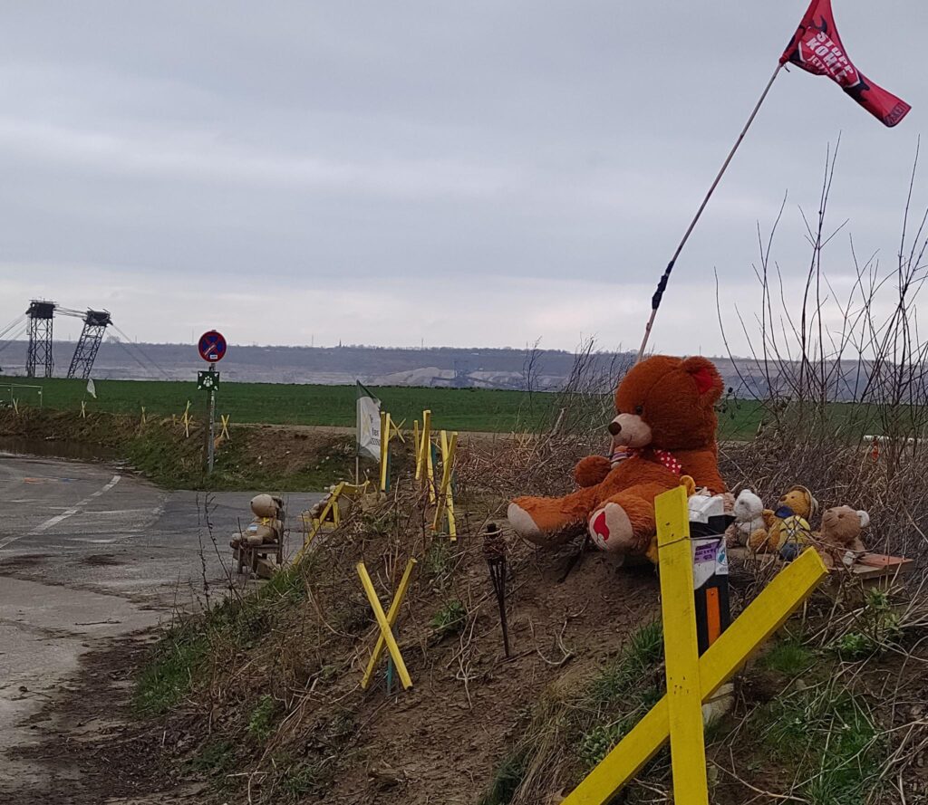 A line of plush toys sit on a hill at the edge of the mine, surrounded by flags and the yellow X-shaped crossbars that symbolise the movement.